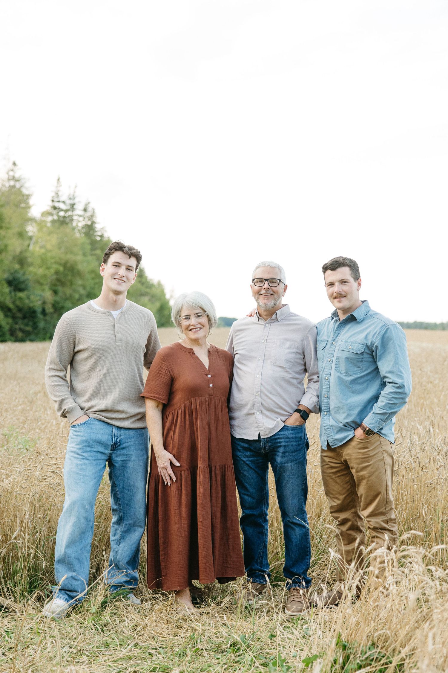 Four adults smile together in golden wheat field, two older and two younger people posing outdoors.