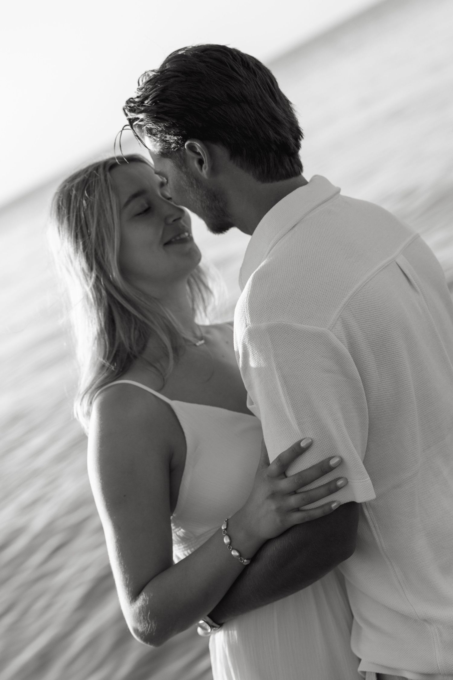 Black and white photo of a romantic couple embracing and almost kissing on a beach.