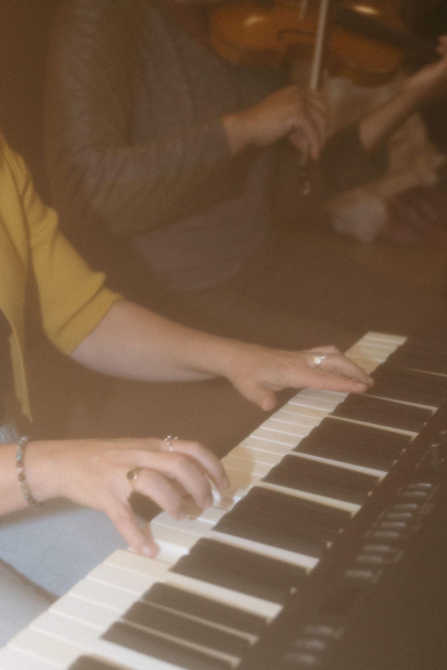 Close-up of a woman's hands playing an electronic keyboard while a violinist plays in the soft-focus background.