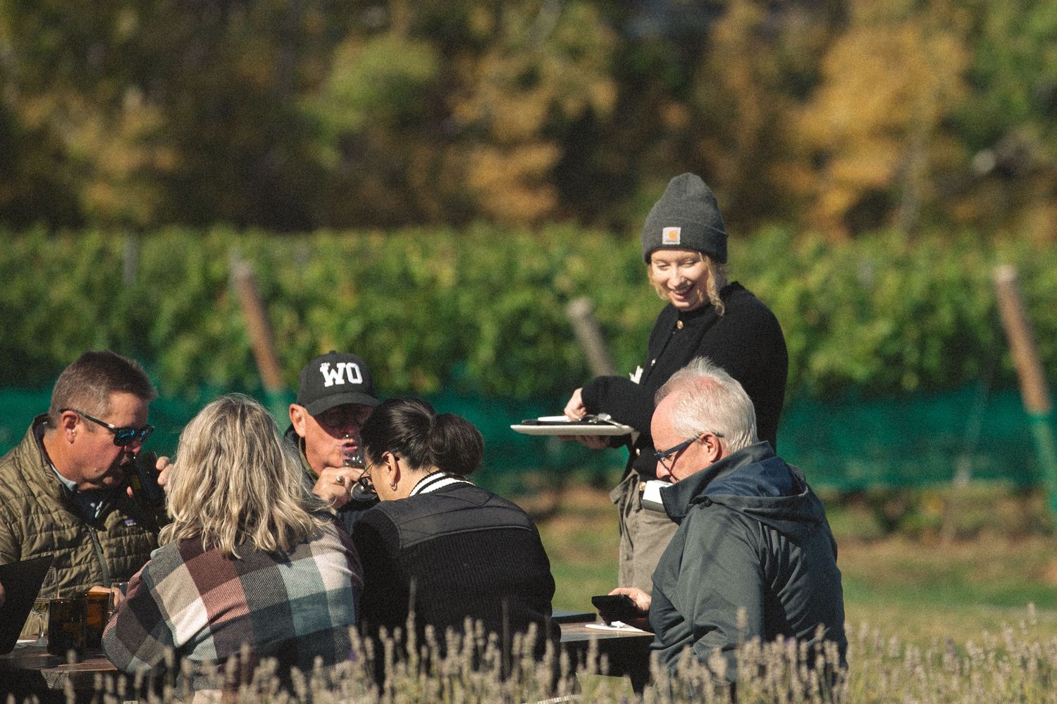 People gathered outdoors at tables for a wine tasting event in autumn.