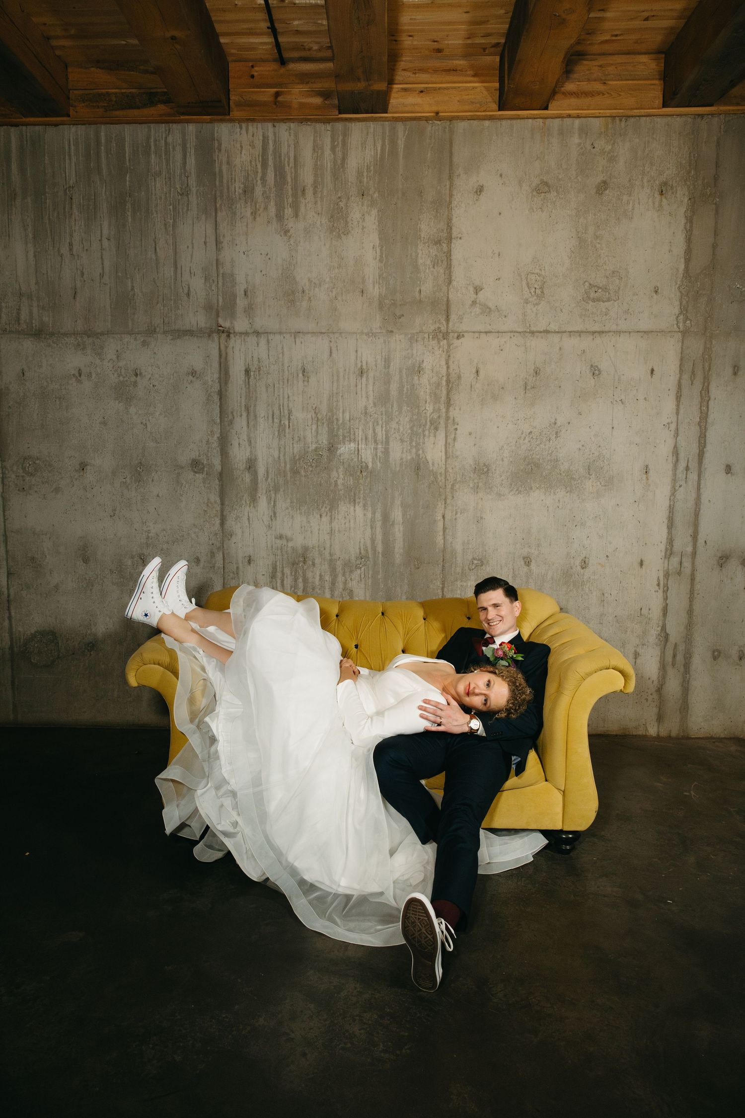 Artistic photo series of wedding couple lounging on yellow couch in industrial space.