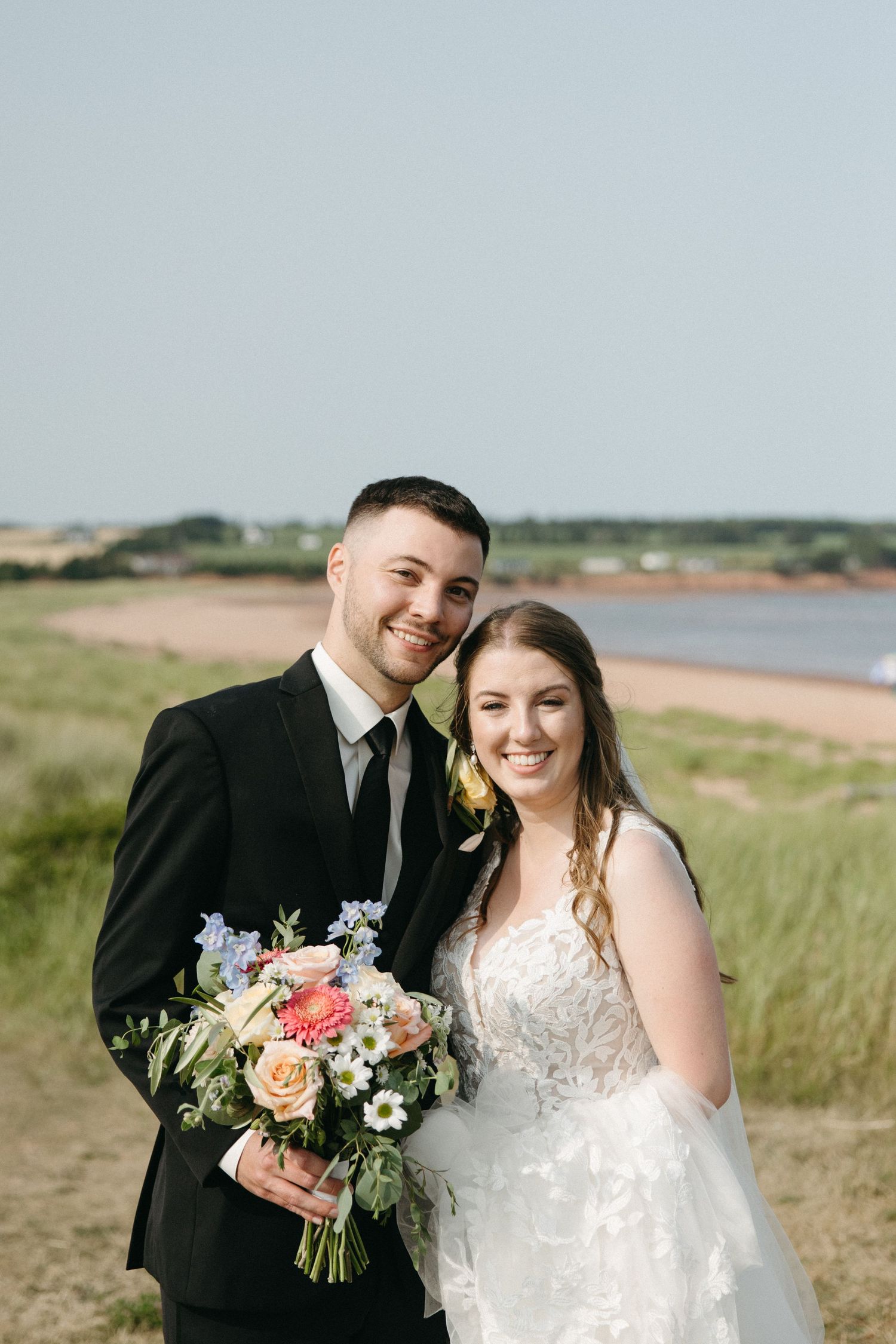 Coastal wedding portraits with couple holding floral bouquet against seaside backdrop.