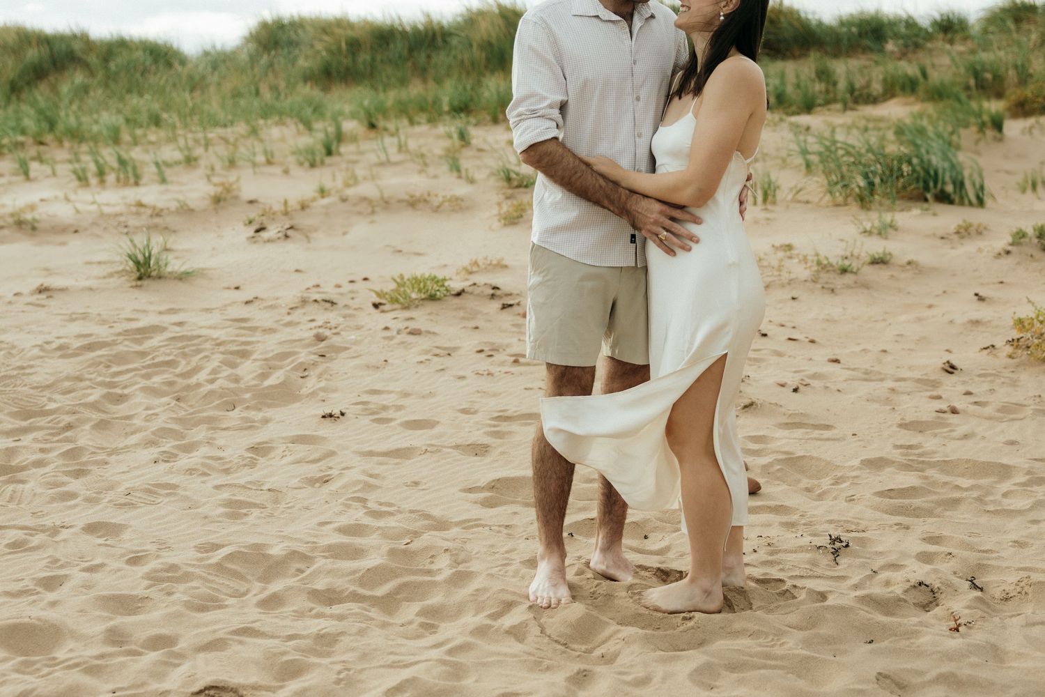Two people in light colored clothing dance together on sandy beach dunes.
