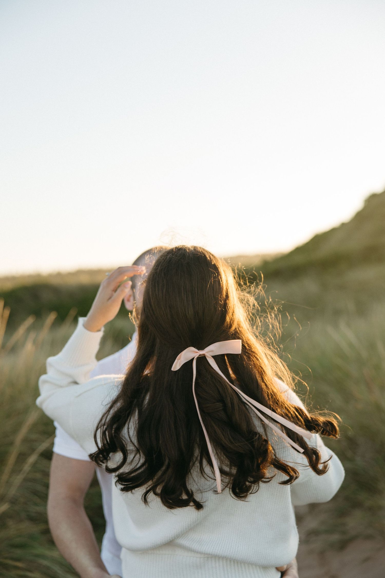 Intimate back view of couple hugging against sunset backdrop.