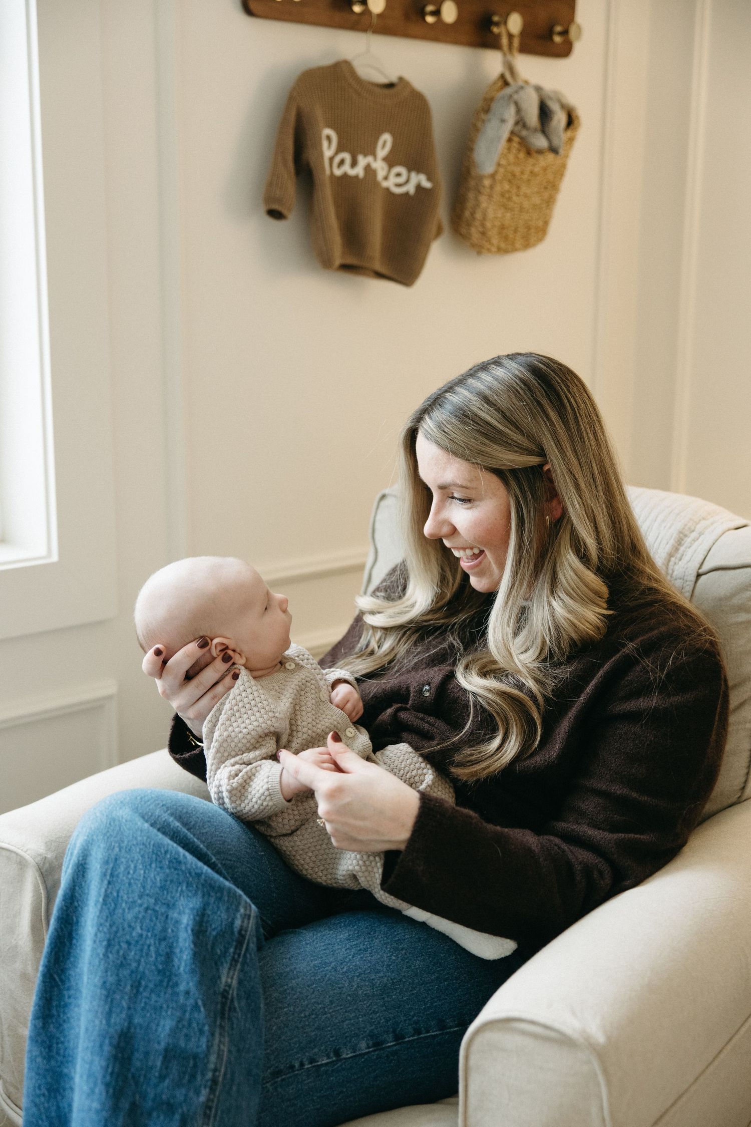 A cozy scene showing a baby in a knit sweater being held on a white couch.