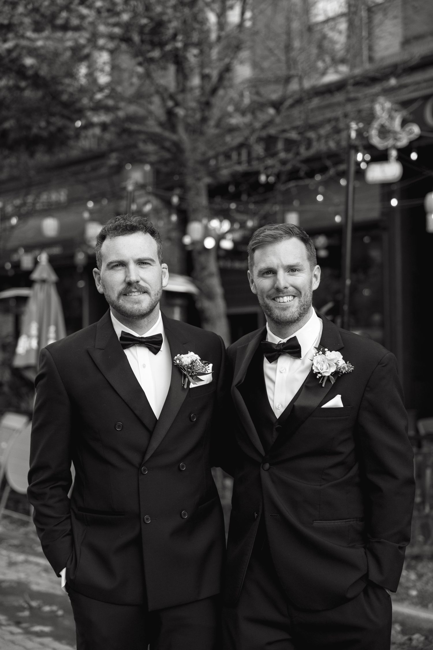 Groomsmen in classic black tuxedos pose outdoors on an autumn day.