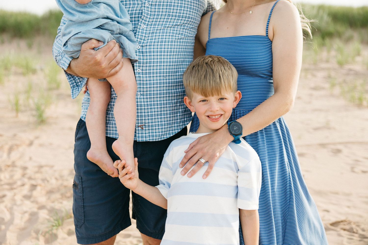 Family portrait on sandy beach with parents holding young children in blue outfits.
