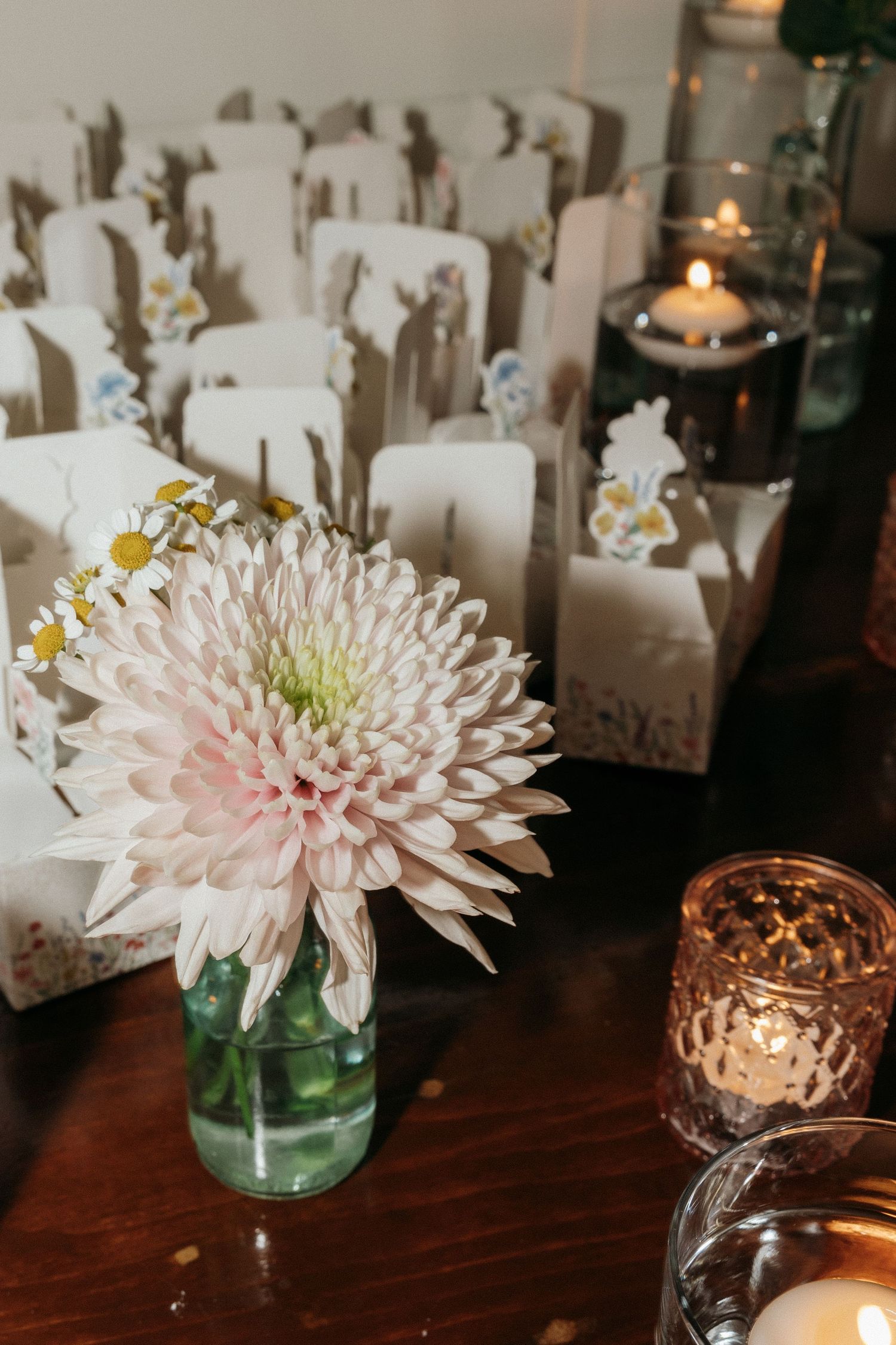 Pink chrysanthemum centerpieces with copper votives and white place cards on dark wooden tables.