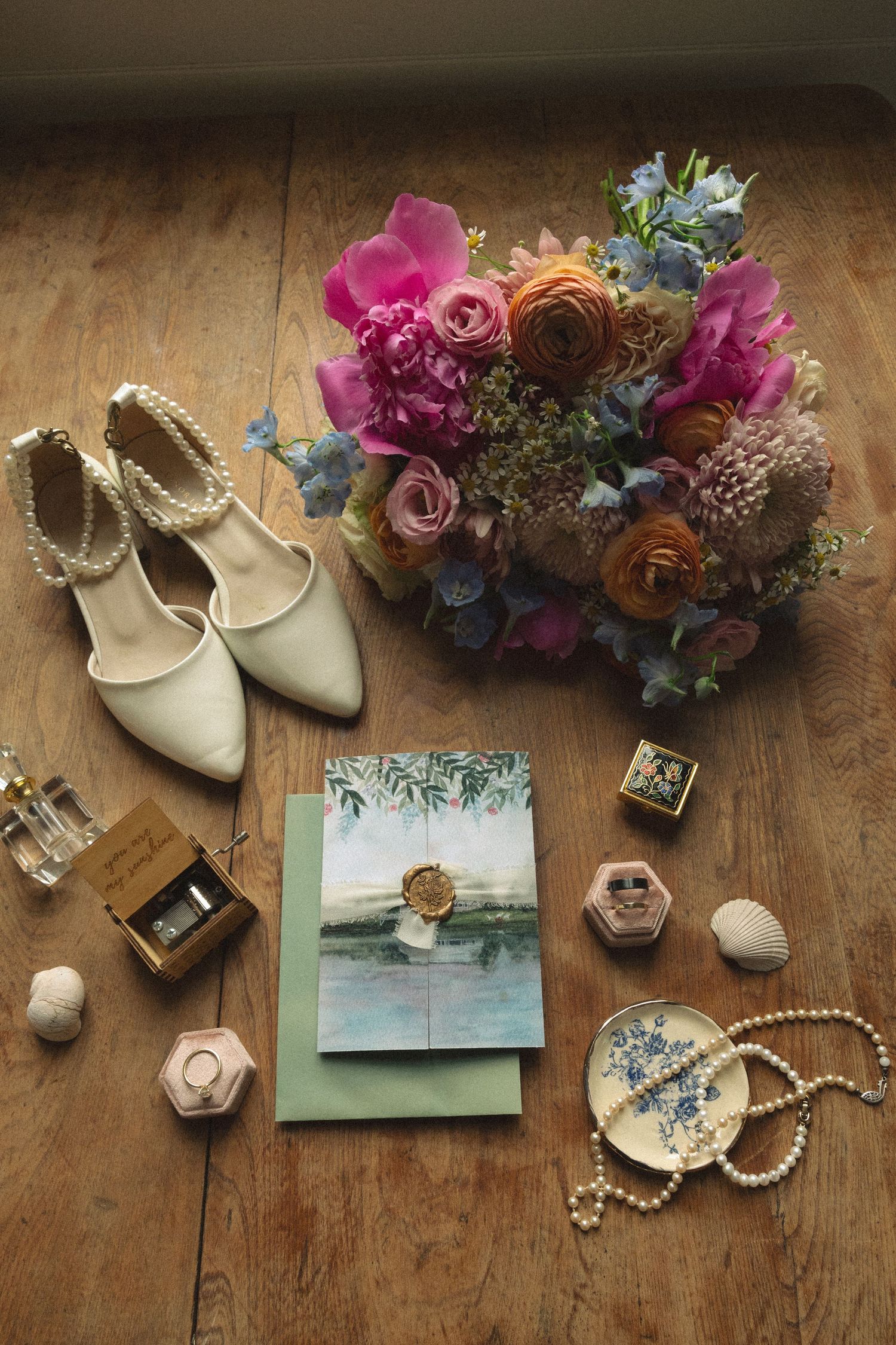 Wedding details flatlay with jewelry, shoes, flowers and stationery on rustic wooden surface.