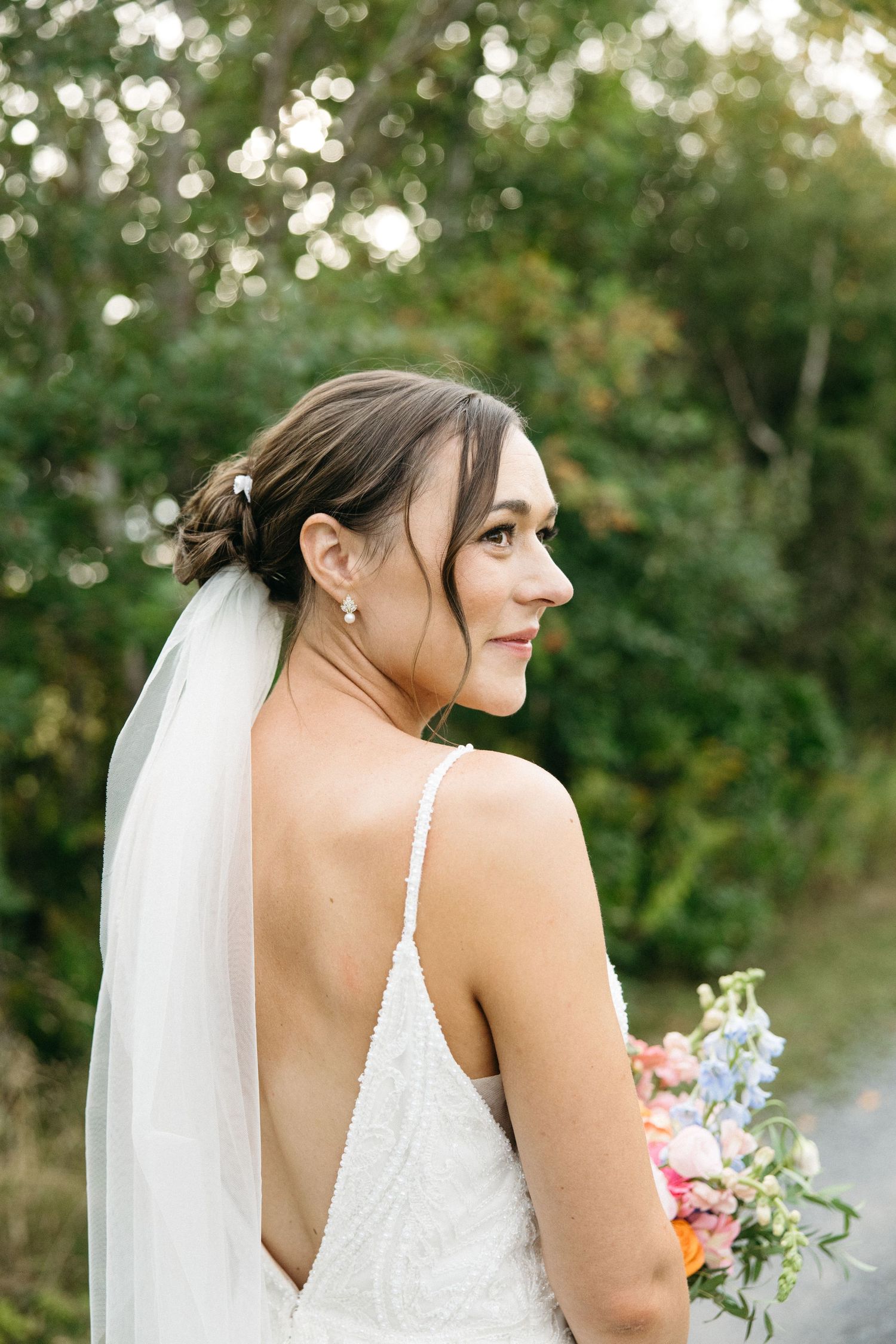 Side profile of bride in lace wedding dress with veil against green foliage background.