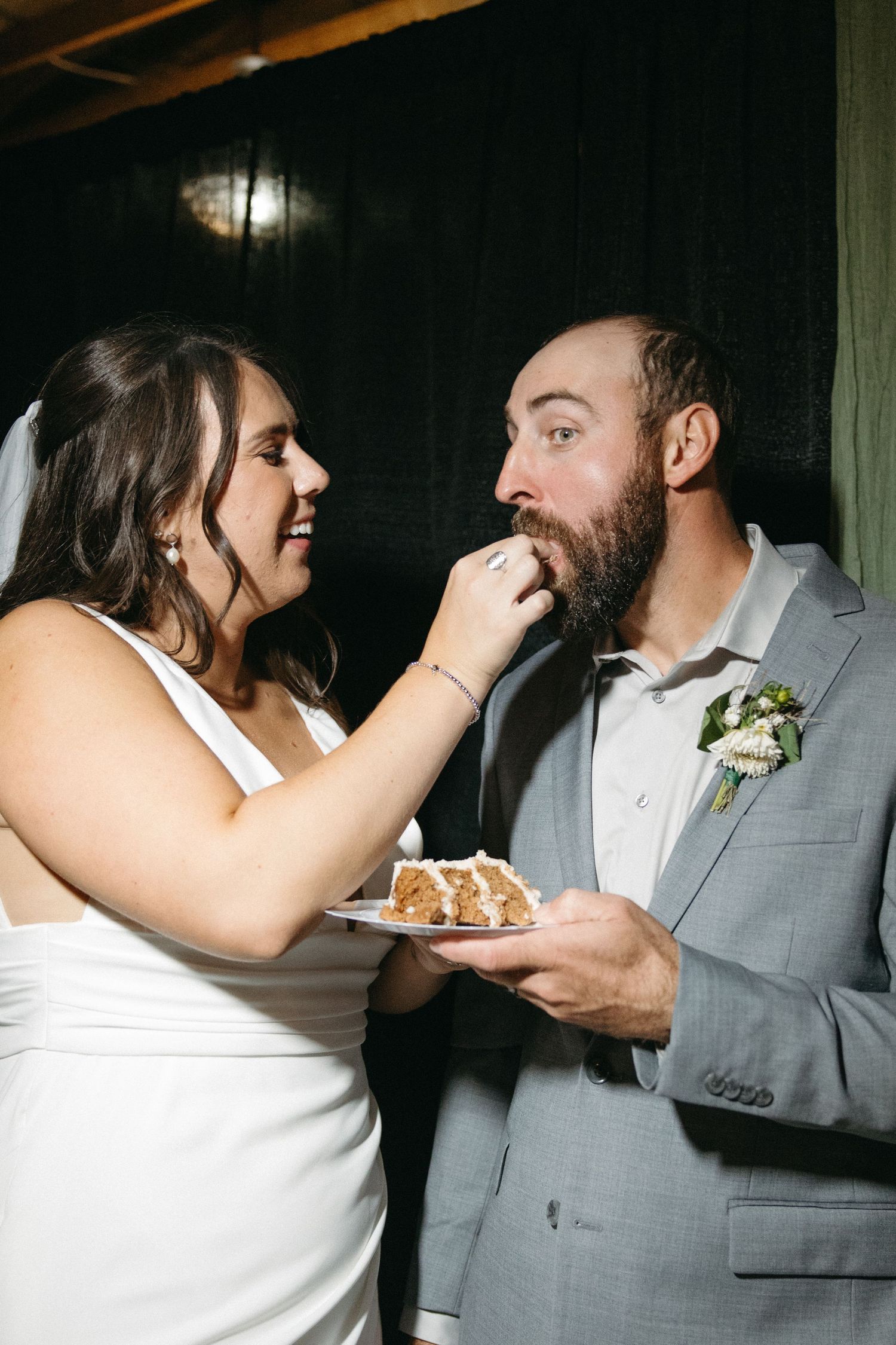 Wedding couple laughs while feeding each other cake during their reception celebration.