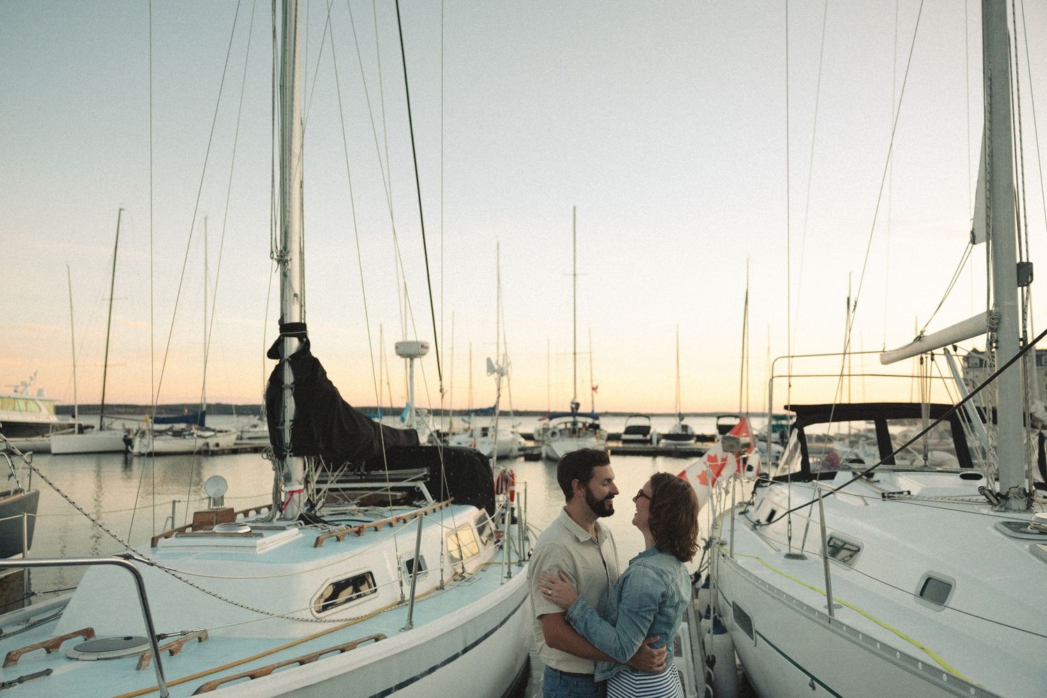A romantic moment shared on a sailboat dock at sunset with boats in the harbor.