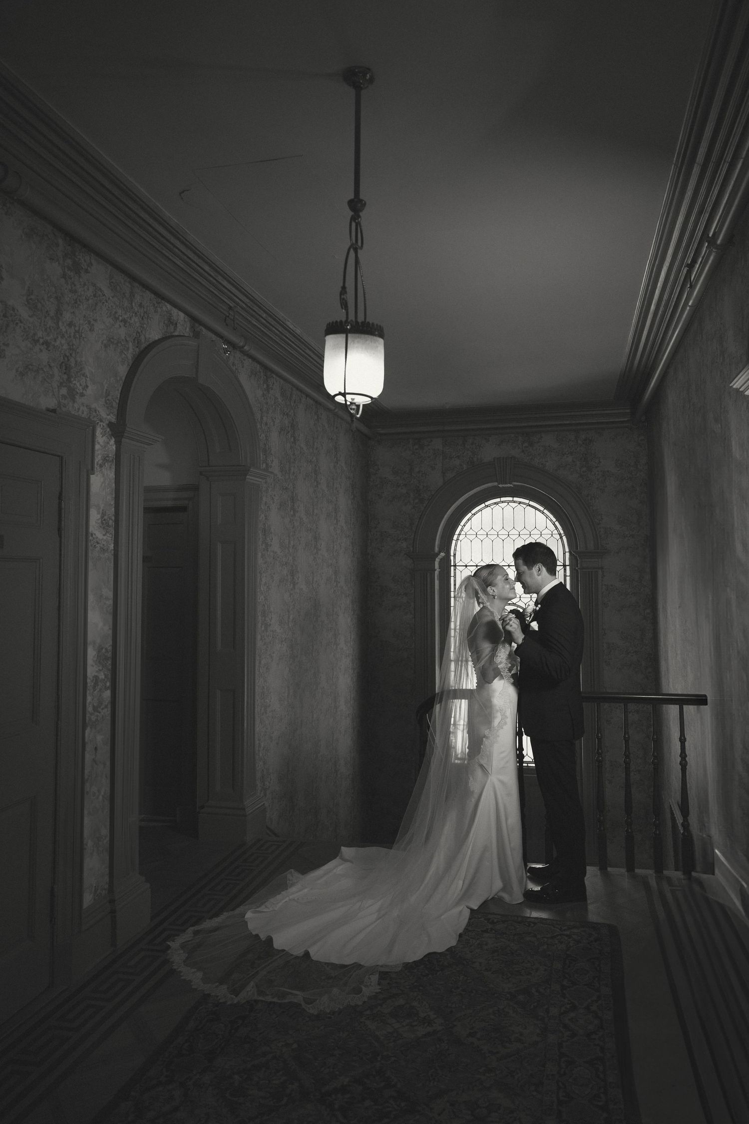 Dramatic black and white wedding photos in a hallway with vintage lighting and architectural details.