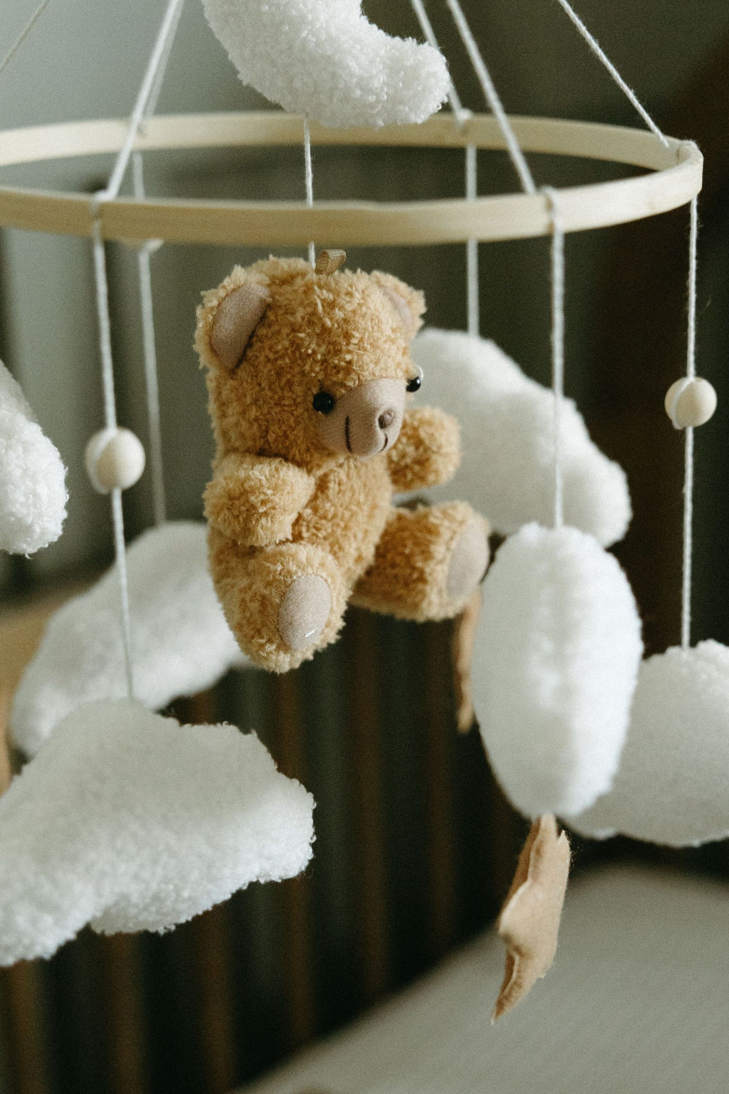 A baby mobile with white plush clouds and teddy bears hanging above a crib.