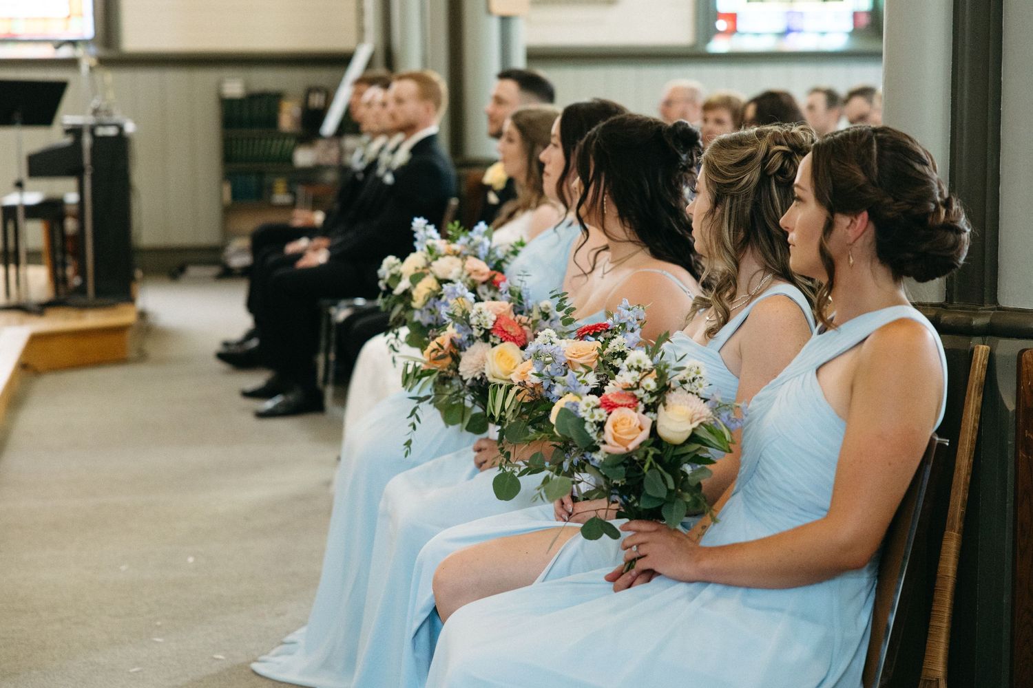Wedding party in light blue dresses holding pink and white floral bouquets in a church.