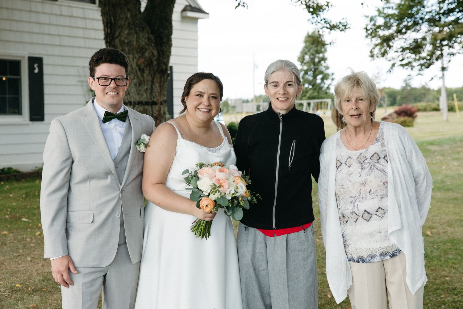 Bride and groom posing with two elderly female relatives outside a white chapel on their wedding day.