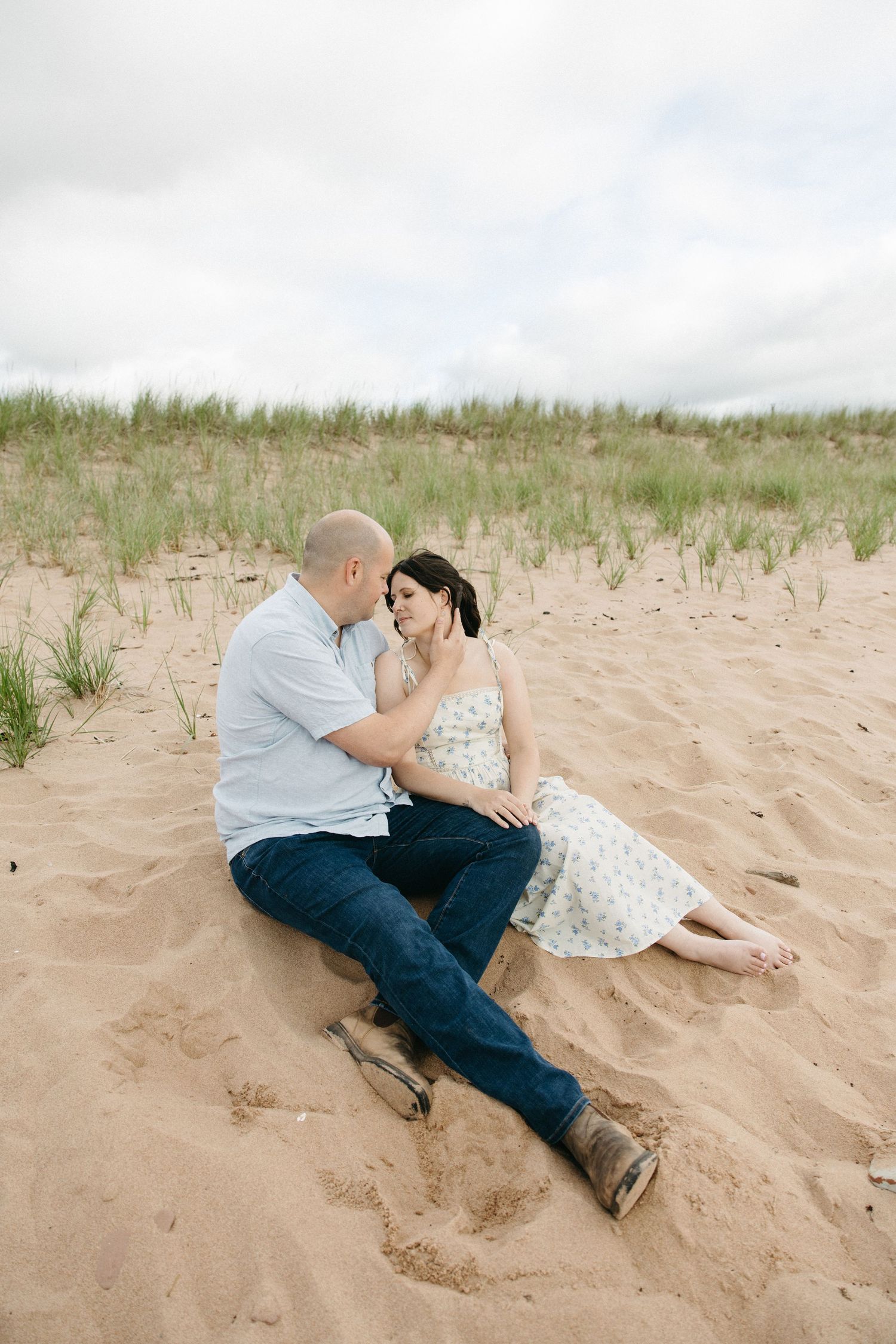 A couple sits together on sandy beach dunes sharing a close romantic moment outdoors.