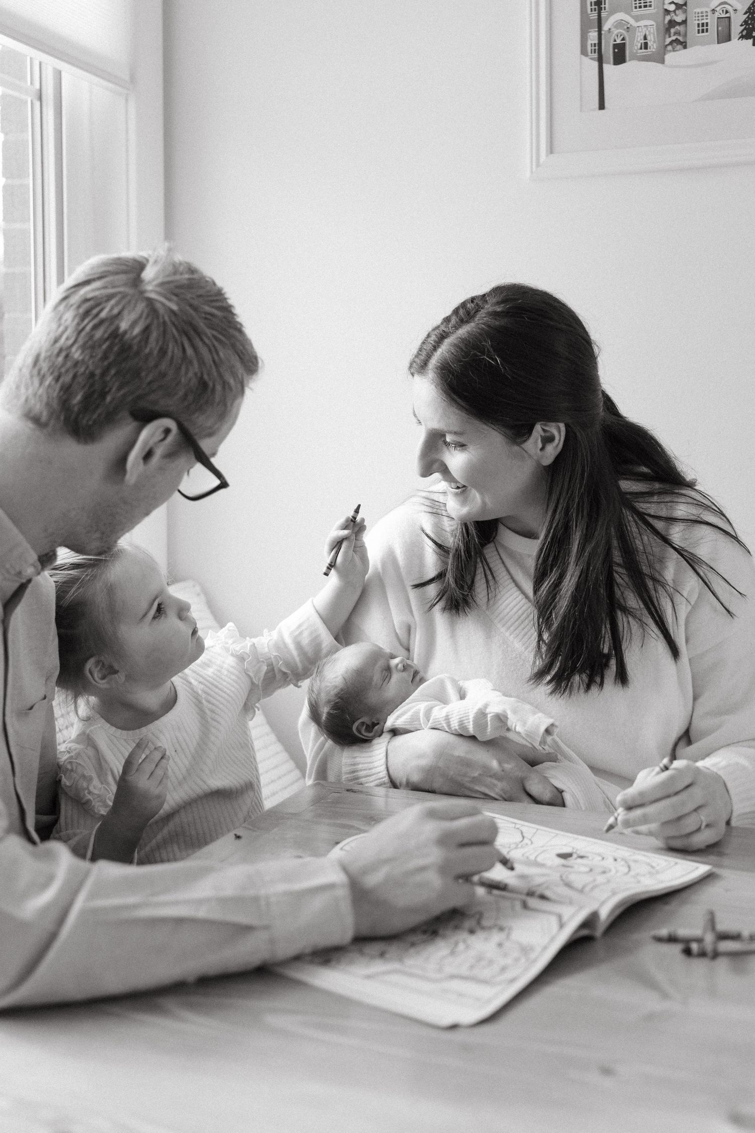A family leans in close together over a table in black and white photography.