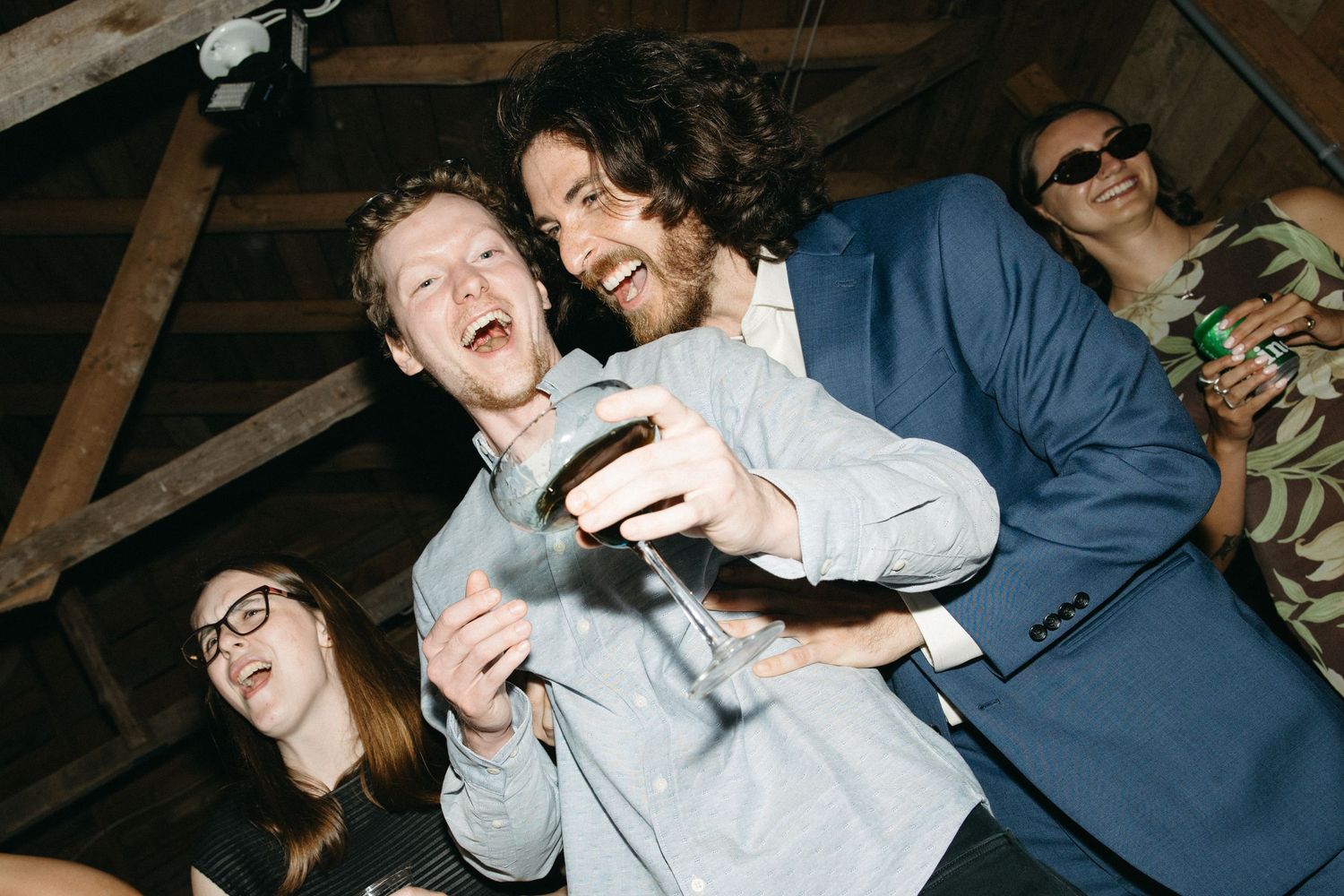 Group of friends laughing and celebrating at a party, man in blue suit holding a drink indoors.