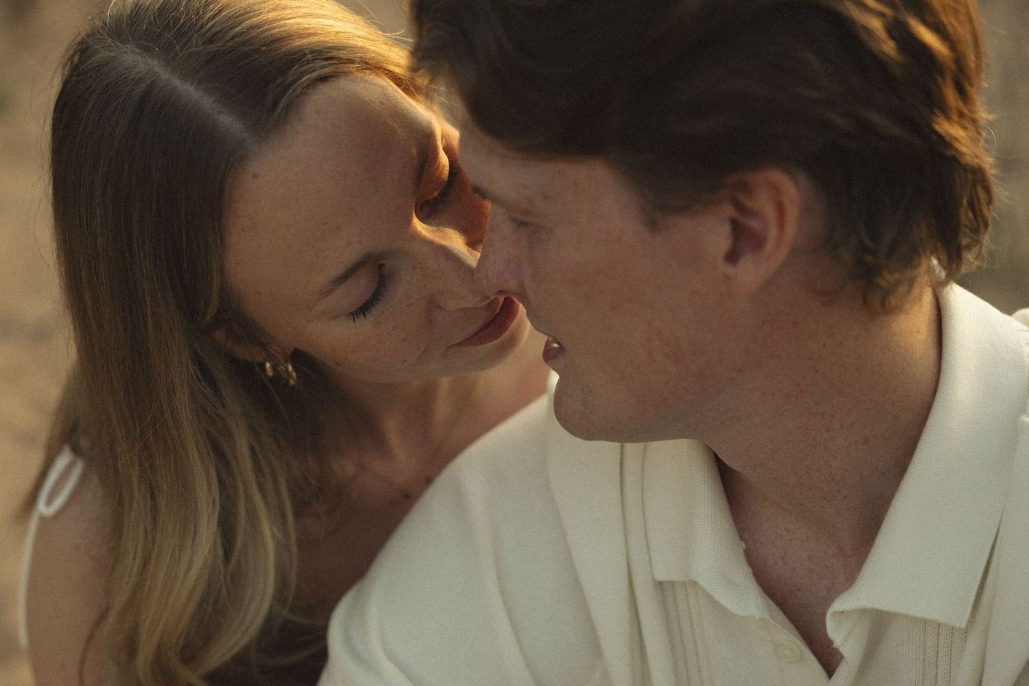 A romantic couple shares an intimate moment, almost kissing, bathed in warm golden light.