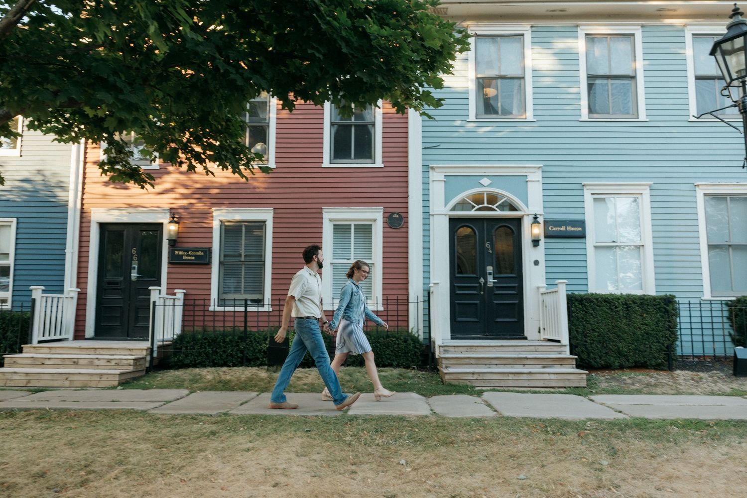 A couple walks past colorful row houses with black doors and white trim on a residential street.