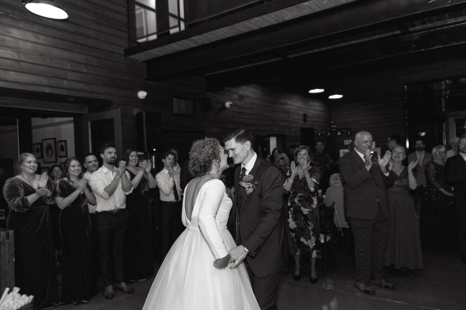 Wedding celebration on a dark wooden dance floor with guests dancing in the background.