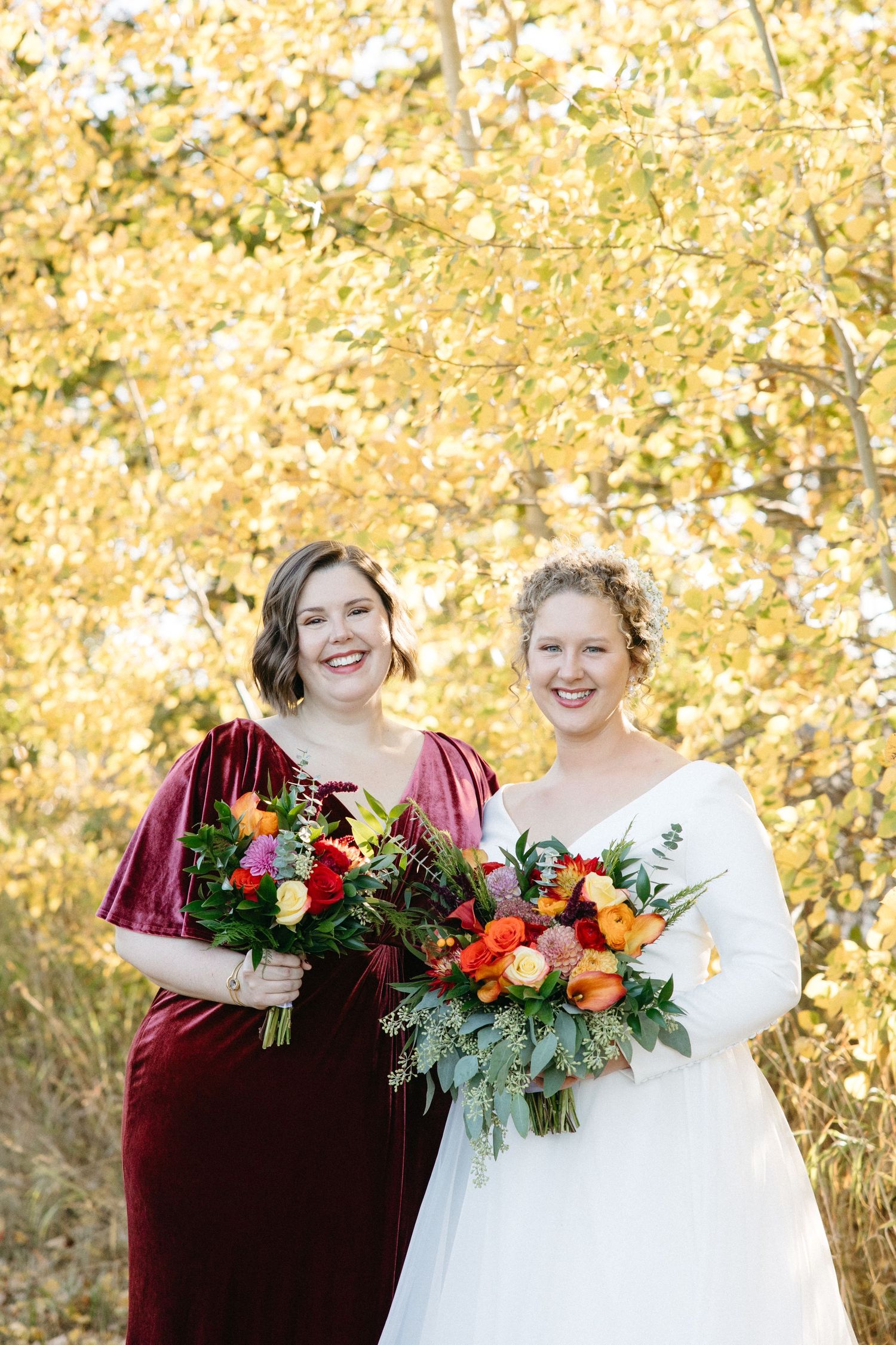 Wedding portrait with burgundy and white attire holding vibrant fall bouquets.