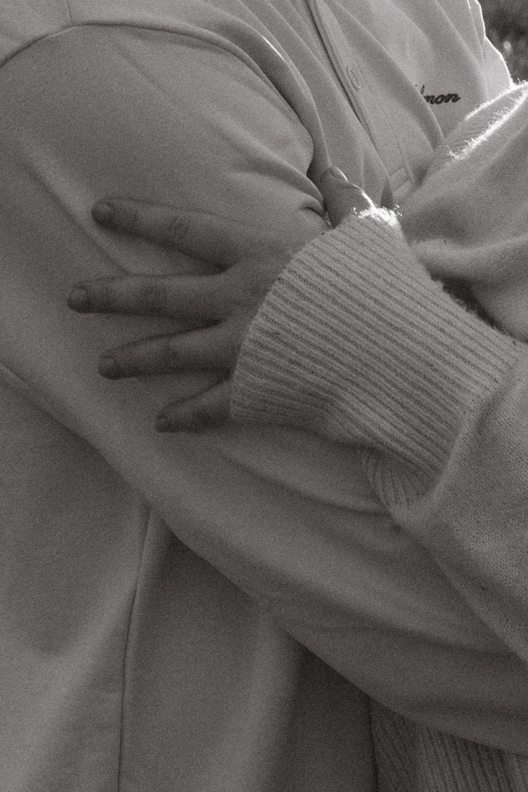Close-up of hands in white knit sweater sleeves crossed over chest.