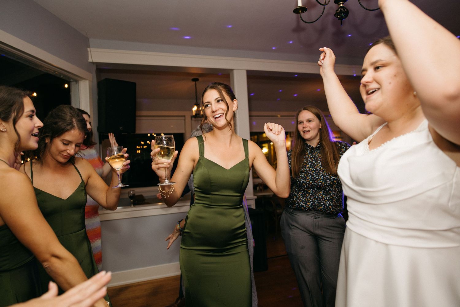 Bride dances joyfully with bridesmaids in green dresses at lively wedding reception celebration.