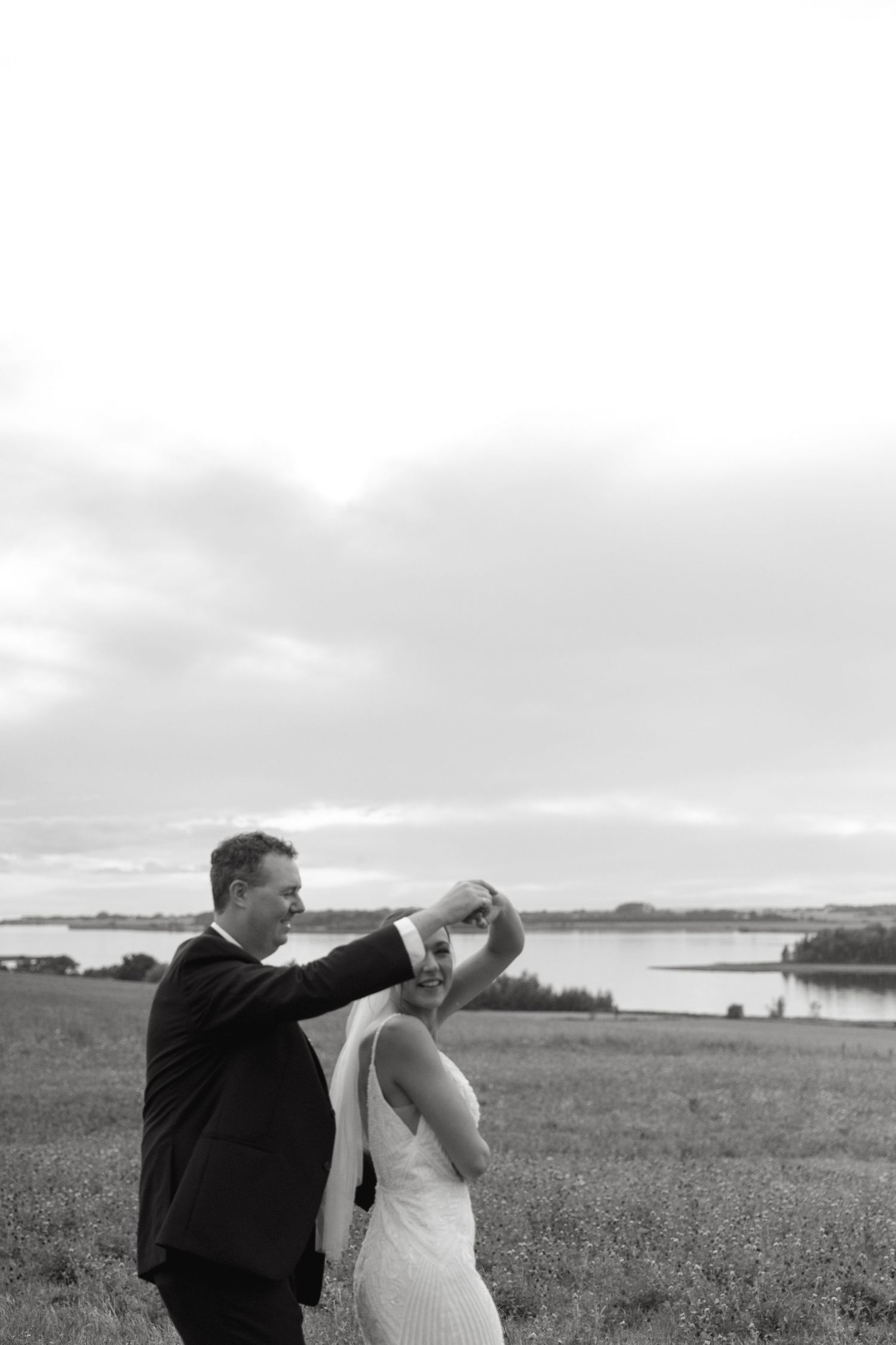 Newlyweds share a romantic moment in a scenic field under overcast skies.