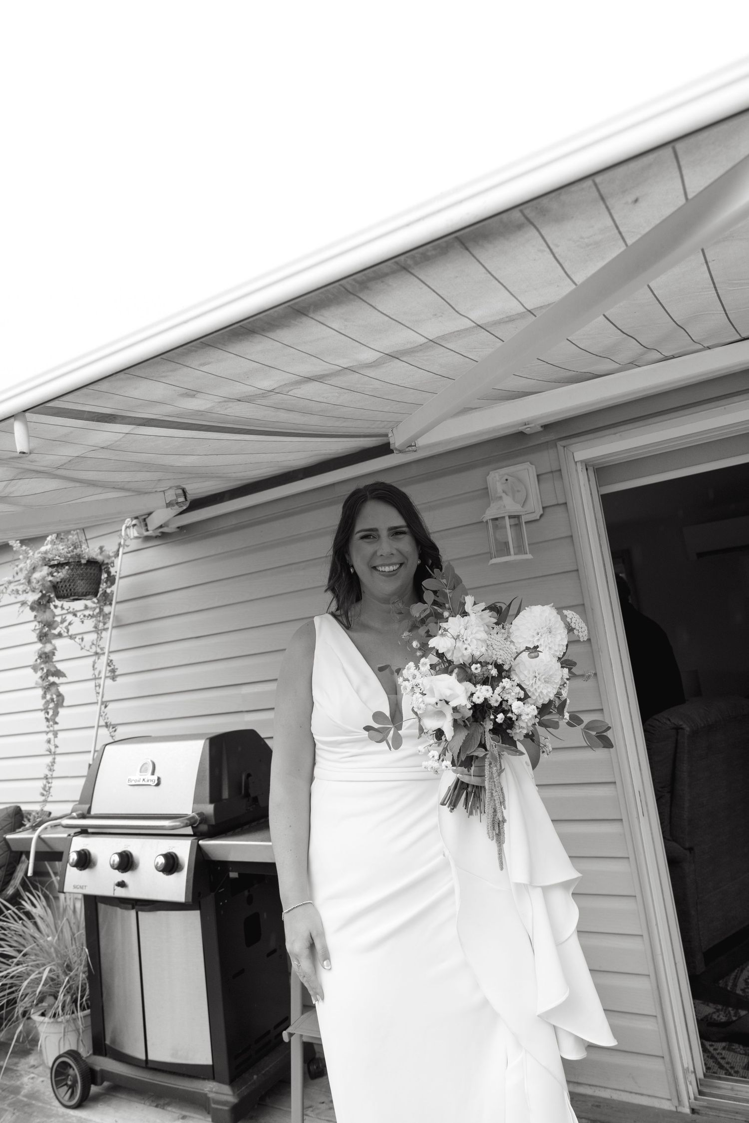 A person in a white wedding dress poses in front of a white house with floral decorations.