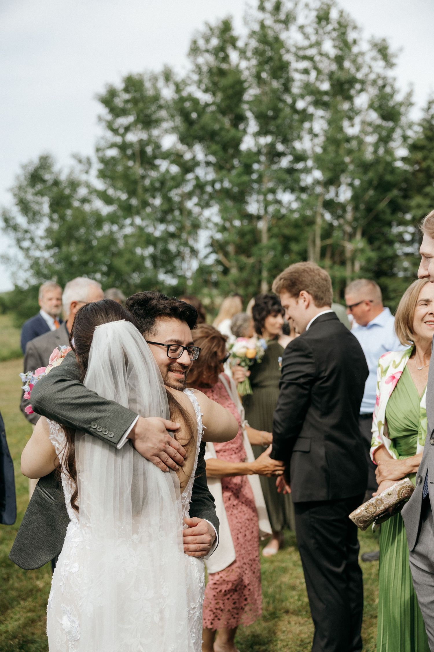 Wedding guests gather outdoors to celebrate and embrace at a joyful outdoor reception ceremony.