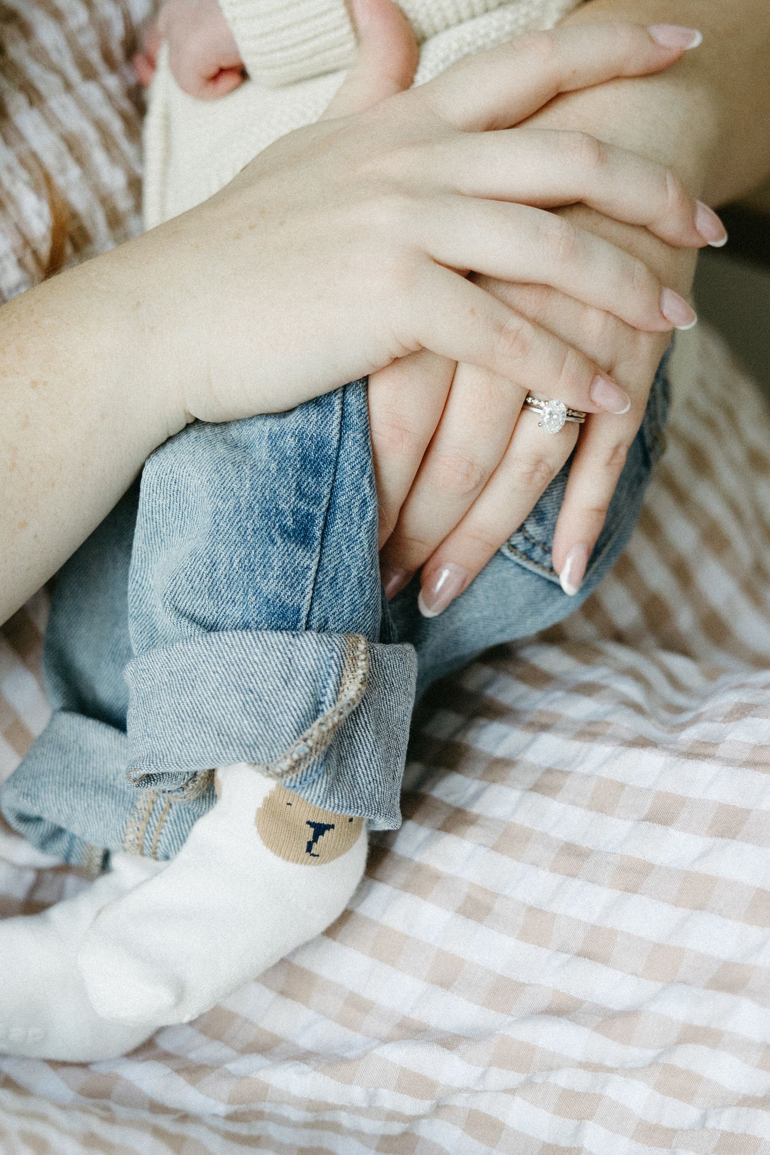 Close-up of hands resting on a checkered blanket with an engagement ring.