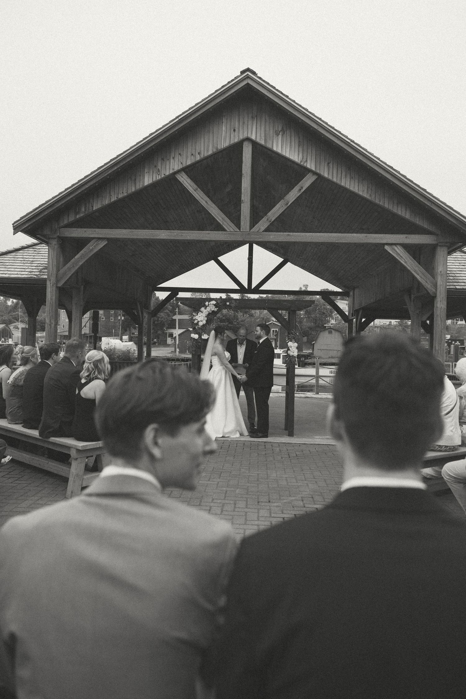 Black and white photo of wedding ceremony under a rustic wooden pavilion.