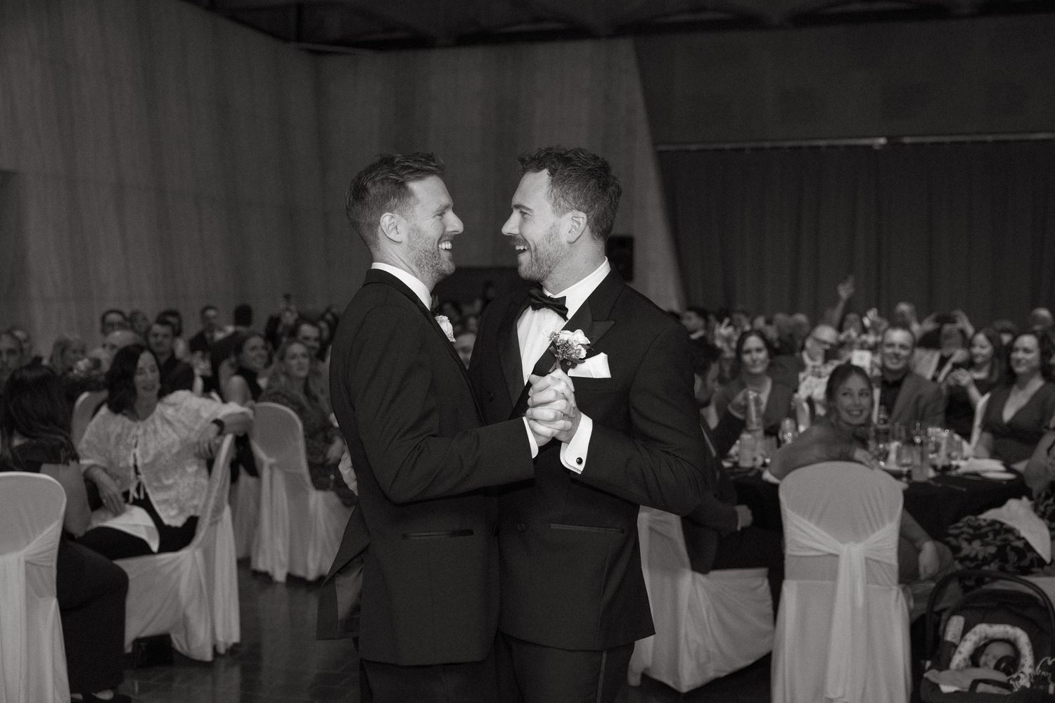 A black and white photo captures a joyful dance celebration at an indoor event.