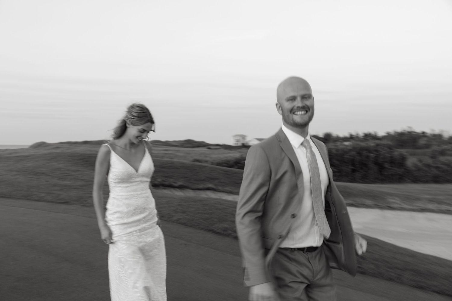 A couple in wedding attire poses together on a scenic coastal overlook.