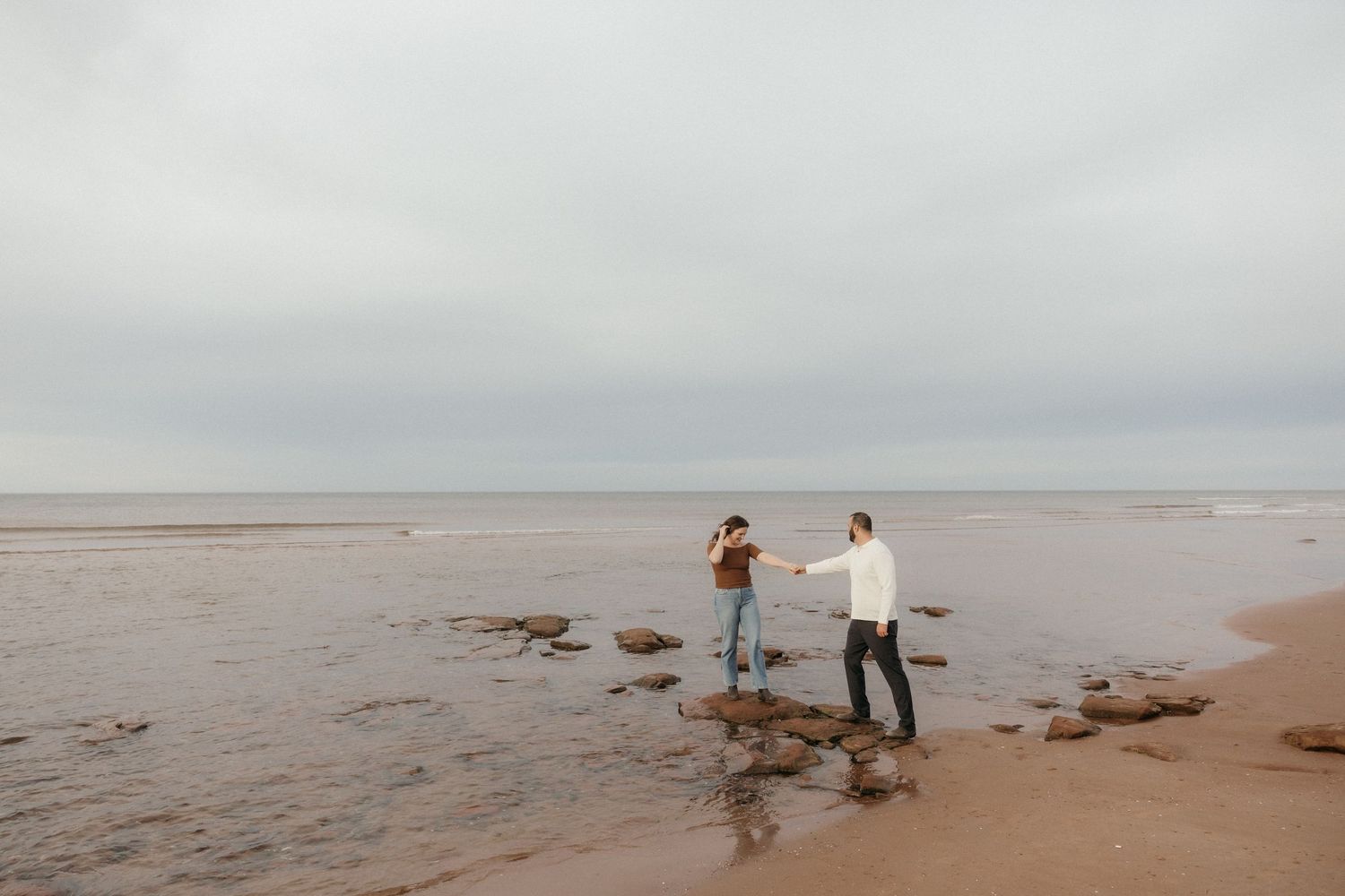 Romantic couple walking along a misty beach shore on an overcast day.