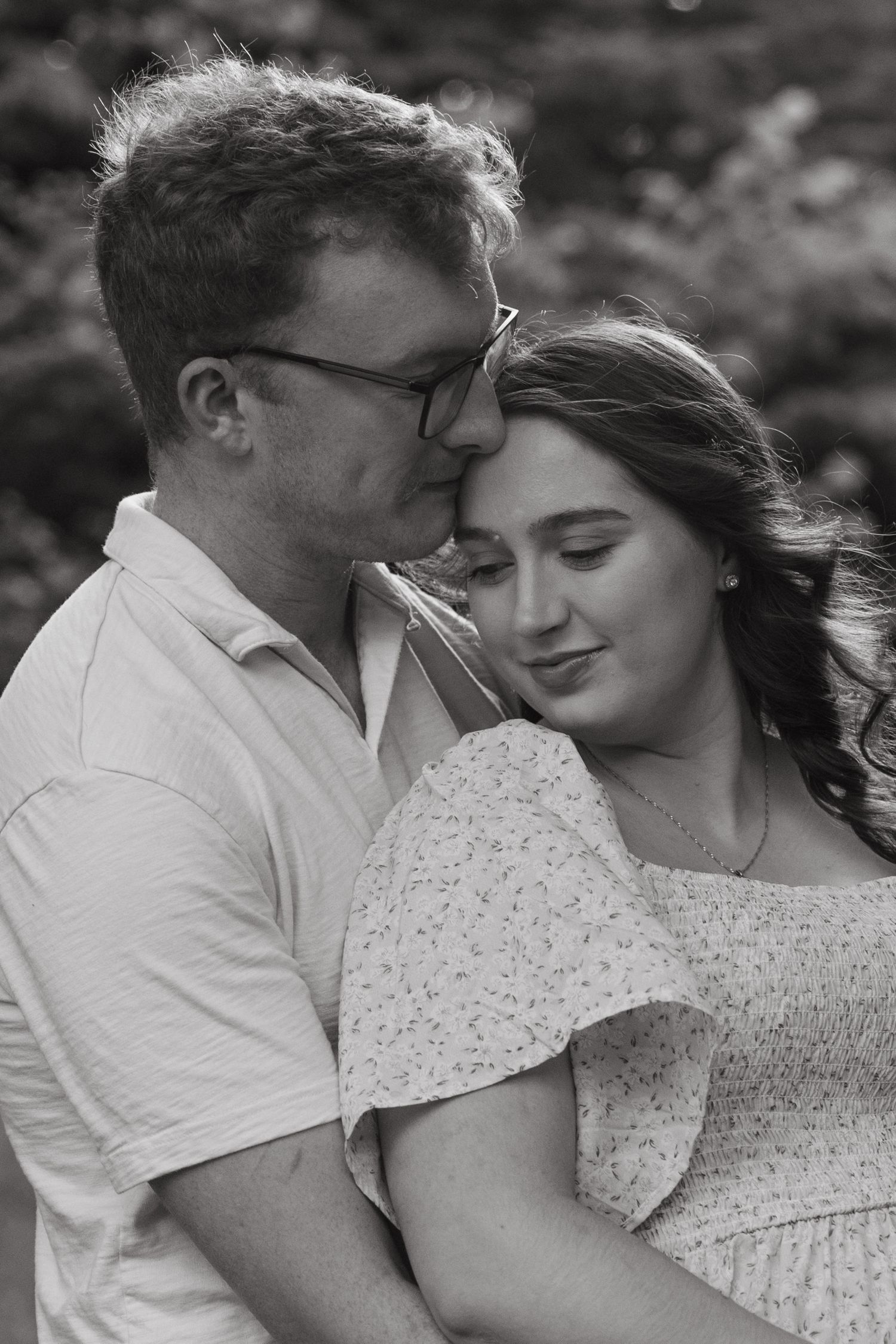 A romantic black and white portrait of a couple sharing an intimate moment outdoors.