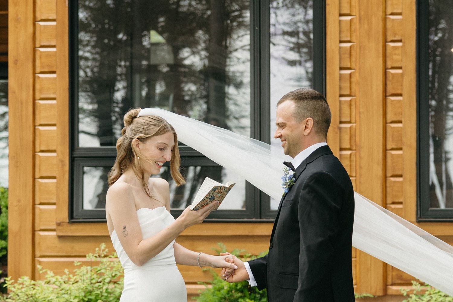 Bride reads heartfelt vows to groom outside rustic wooden building on their wedding day.