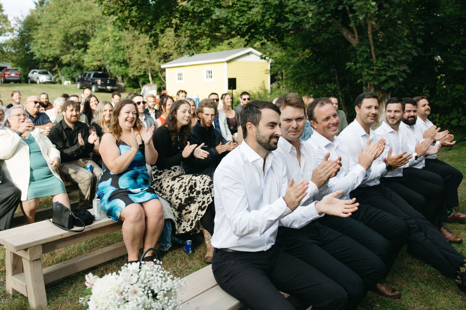 Wedding guests seated on wooden benches during outdoor ceremony.