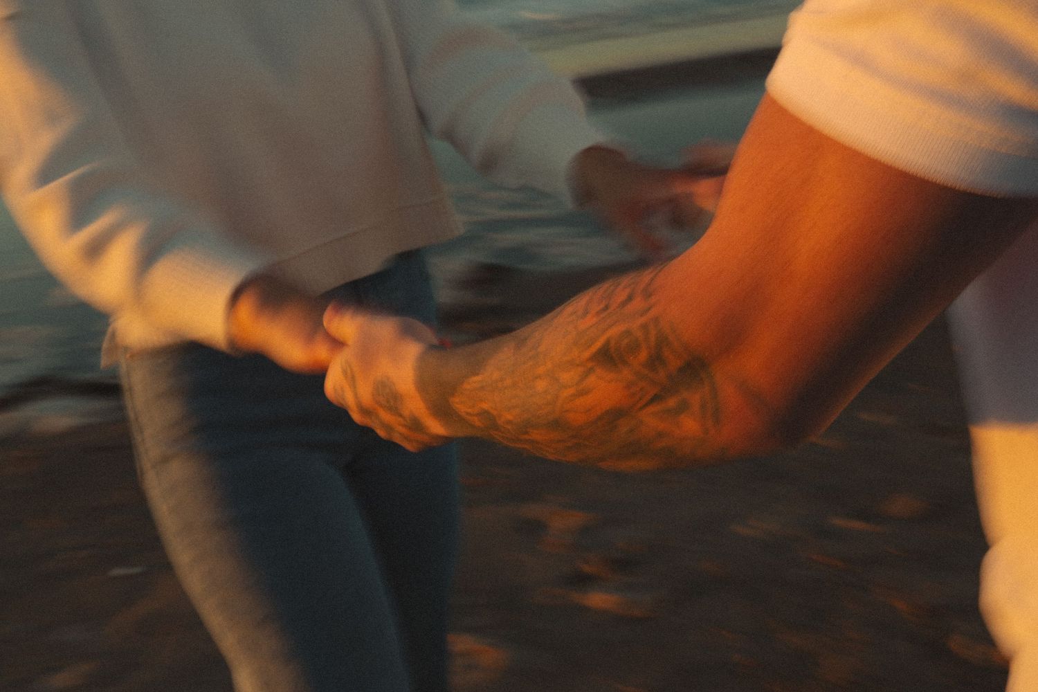 Couple holding hands while walking on sandy beach during sunset.