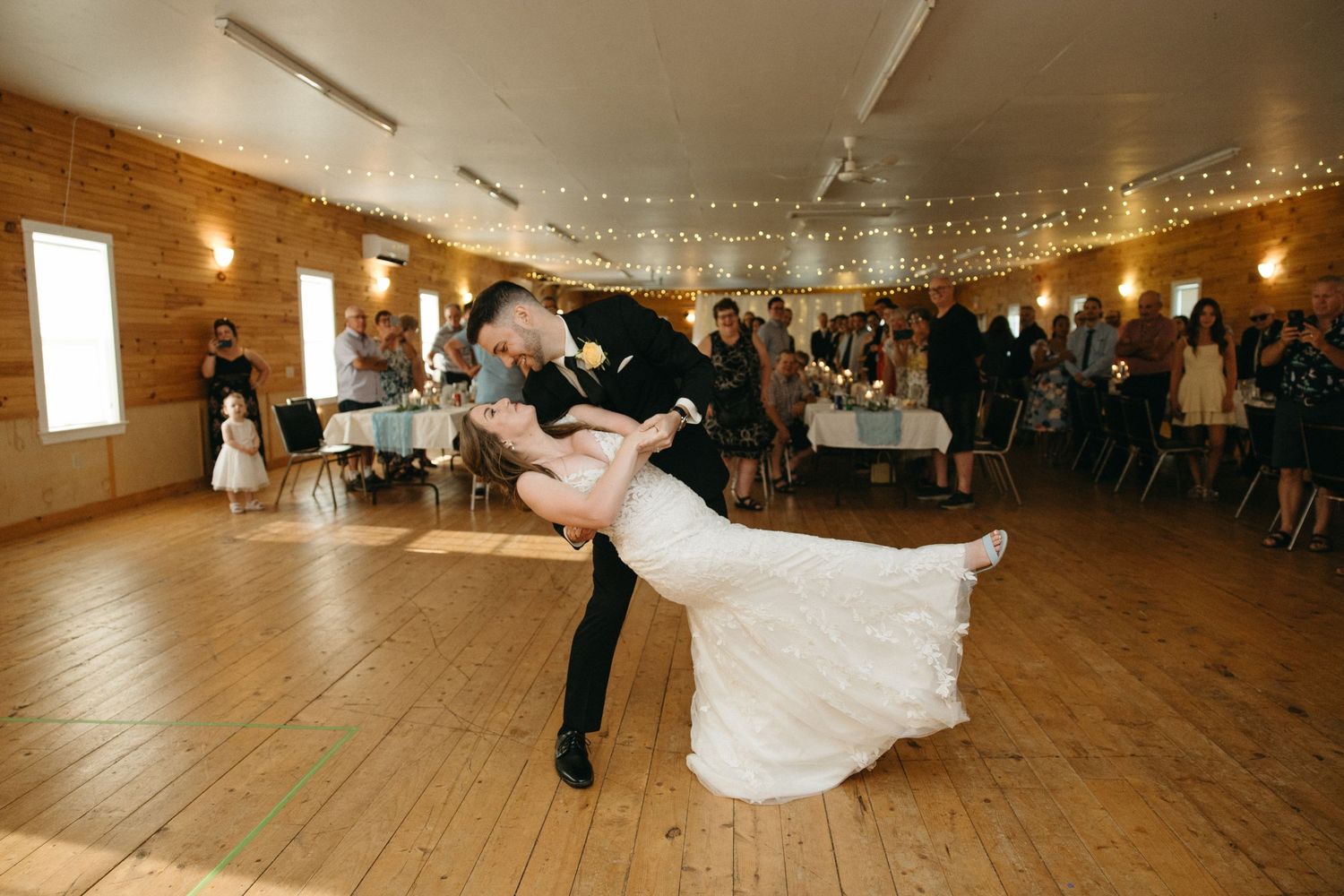 Panoramic view of rustic wooden wedding venue with string lights and dancing guests.
