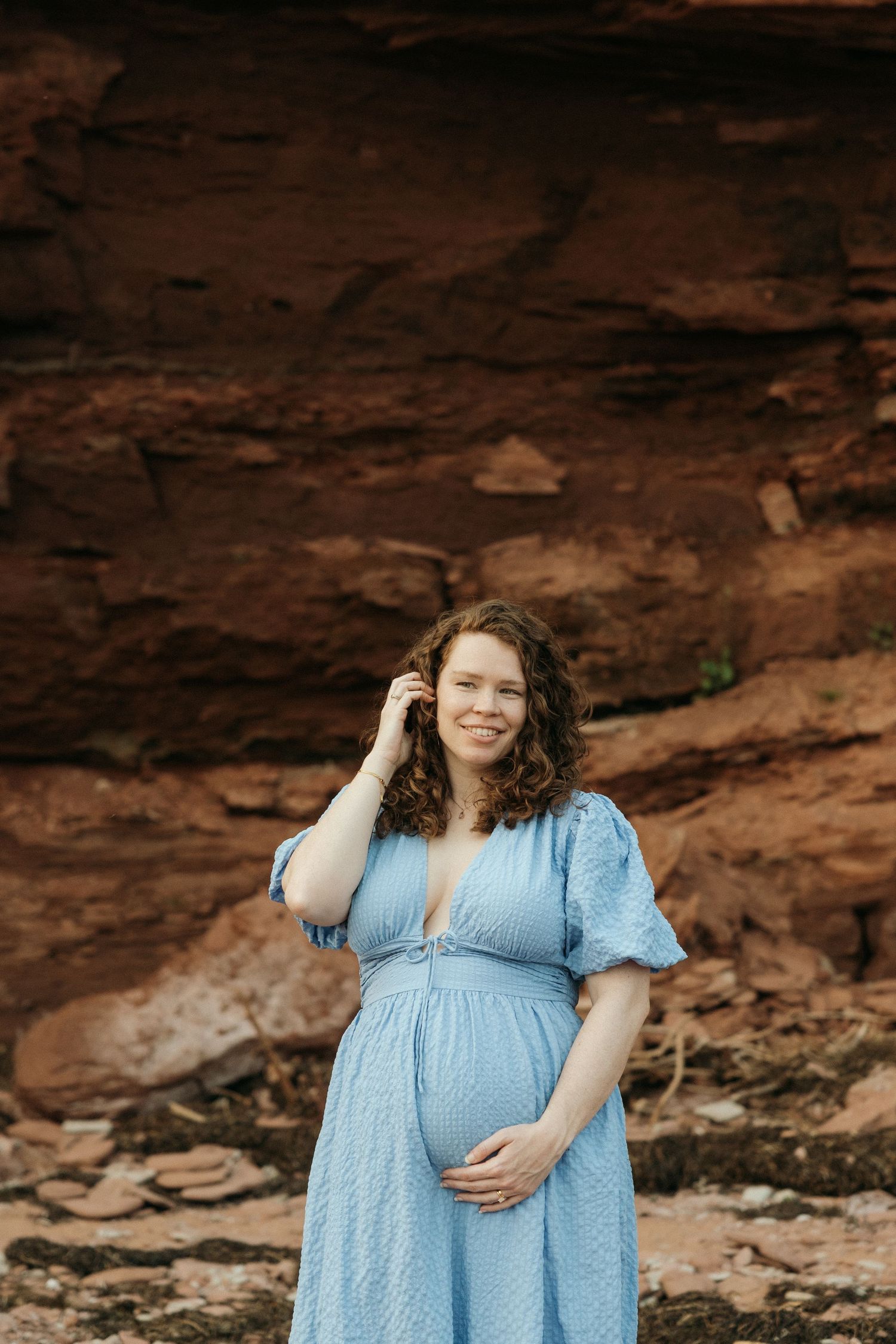 Maternity photos taken against dramatic red rock formations with someone in a light blue dress.
