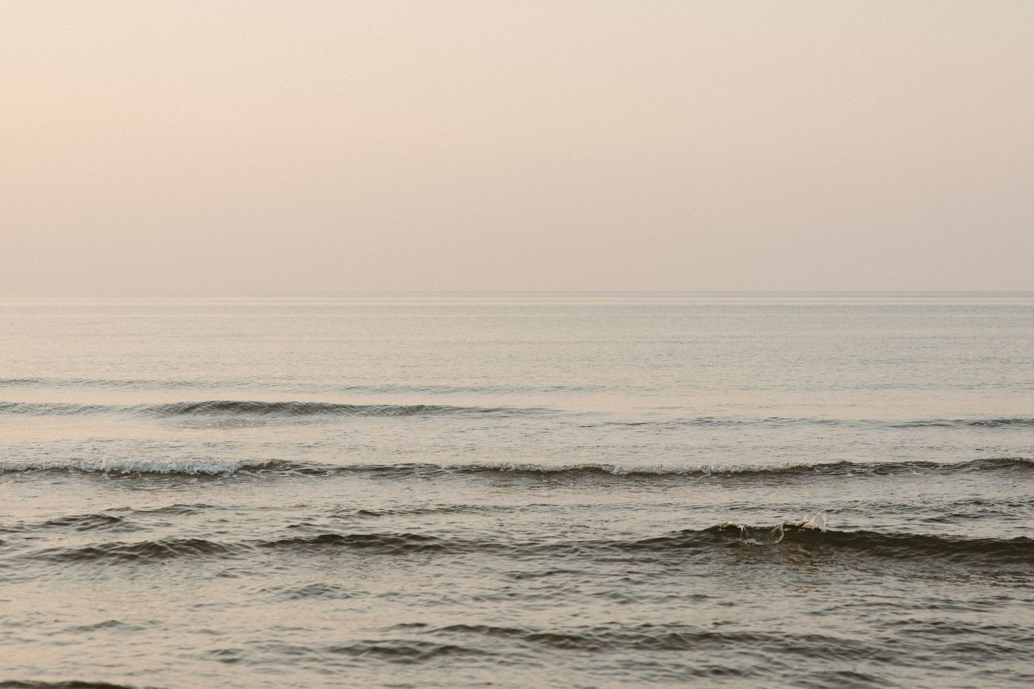 Calm ocean waves gently roll onto shore at dusk under a soft pastel sky.