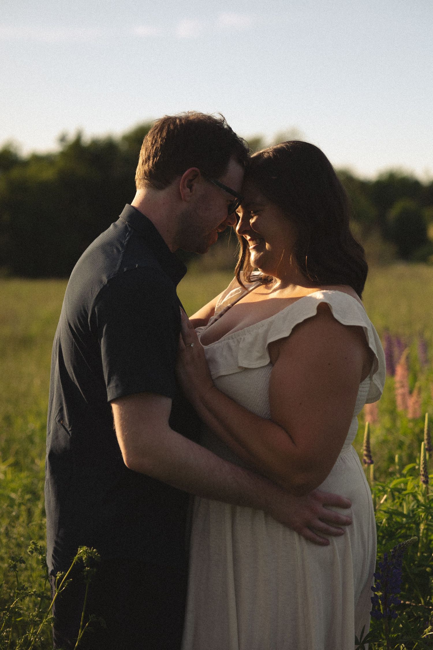 Couple embracing forehead to forehead in wildflower field during warm summer sunset.