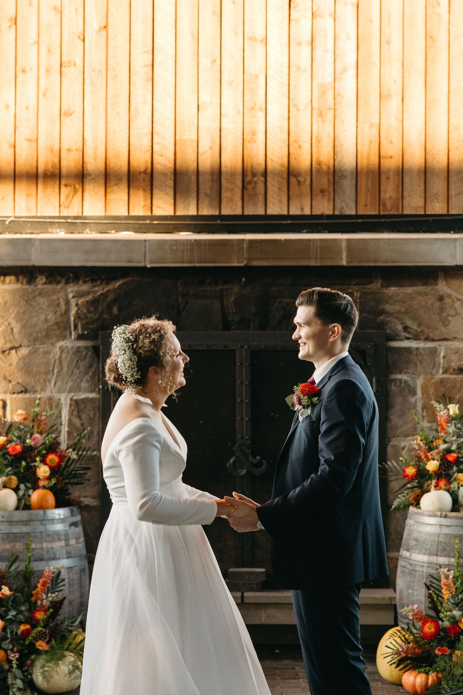 Wedding ceremony in a rustic barn with wooden walls and fall decorations including pumpkins and floral arrangements.
