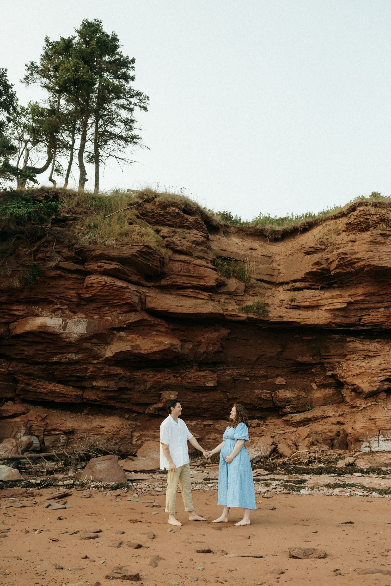 Couple walking hand in hand along a dramatic red sandstone cliff face on a beach.