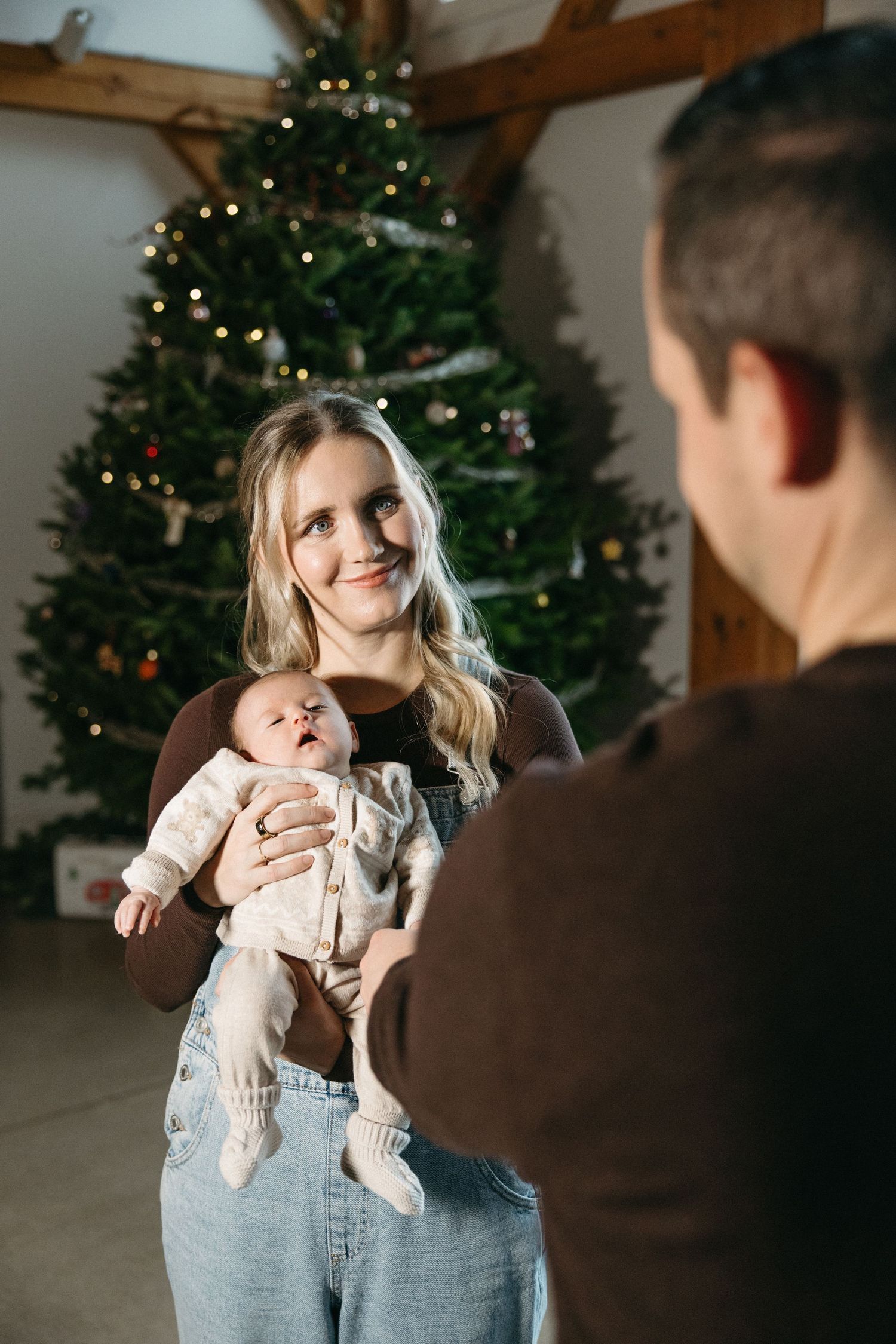 A tender family moment in front of a Christmas tree with a baby in light colored clothing.