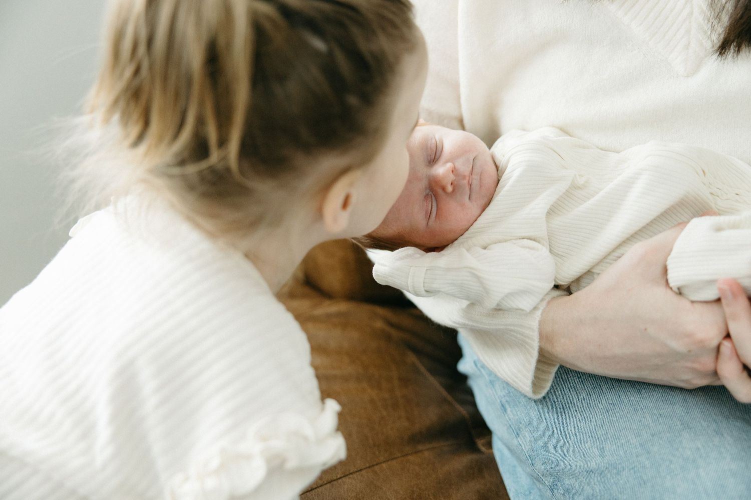 Gentle interaction with a newborn baby swaddled in white fabric against a wooden surface.