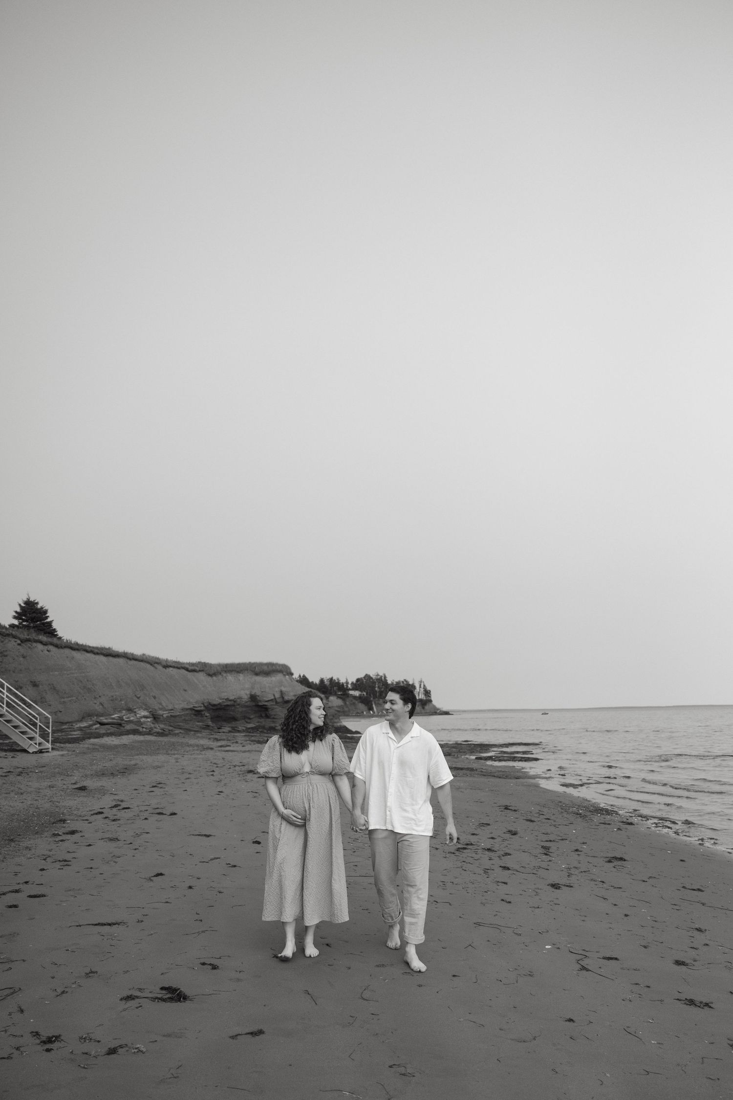Black and white photo of two people walking hand in hand on a remote beach.